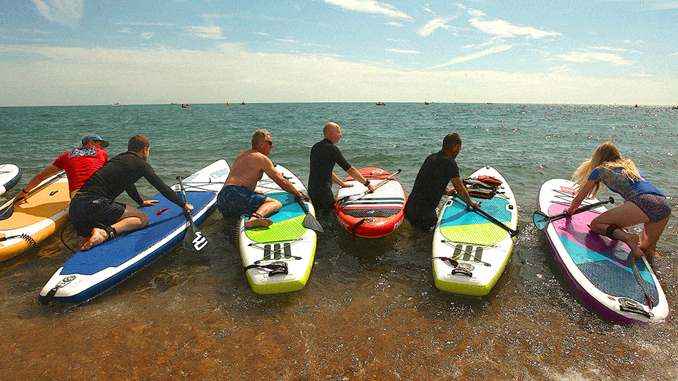 Grupo de hombres a partir de tablas de paddle en la playa